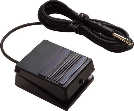 The image shows a black sustain pedal with a ribbed surface and attached cable ending in a 1/4" jack plug, secured with a cable tie. Used with electronic keyboards and digital pianos, it mimics an acoustic piano’s damper pedal by sustaining notes after keys are released, enhancing musical expression and playability.