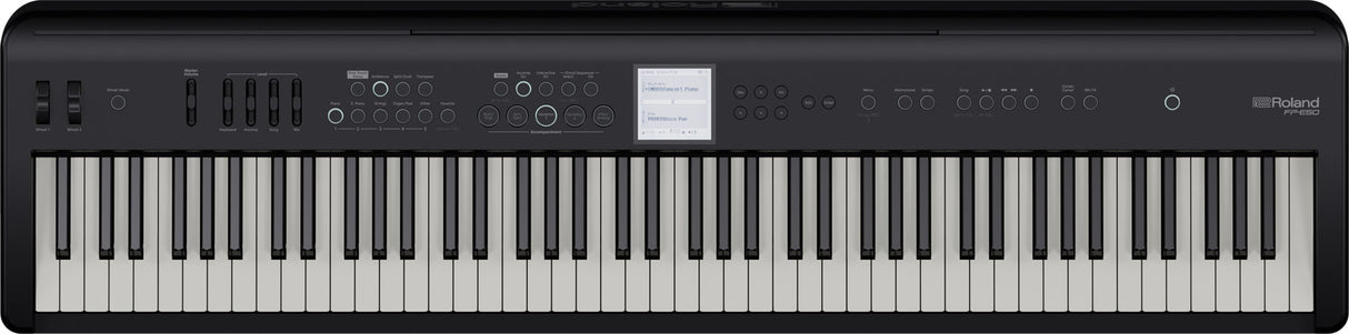 The image shows a Roland digital piano with classic black and white keys in a standard layout. Above the keys is a control panel featuring buttons, sliders, and a small central display screen. The Roland logo is visible in the top right corner. This digital piano replicates an acoustic piano’s feel and sound while offering additional features like multiple instrument voices, recording options, and sound effects.