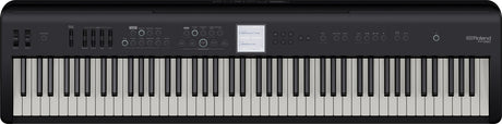 The image shows a Roland digital piano with classic black and white keys in a standard layout. Above the keys is a control panel featuring buttons, sliders, and a small central display screen. The Roland logo is visible in the top right corner. This digital piano replicates an acoustic piano’s feel and sound while offering additional features like multiple instrument voices, recording options, and sound effects.