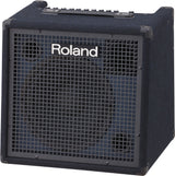 The image shows a Roland keyboard amplifier with a cube-style, compact design and dark blue textured exterior. It features a metal grille front with Roland branding, a top control panel with multiple knobs, a carrying handle, and reinforced corners. This professional, portable amp is designed for amplifying electronic keyboards and digital pianos, suitable for practice, rehearsal, and live performance.