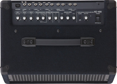 The image shows a Roland KC-400 Stereo Mixing Keyboard Amplifier, designed for electronic keyboards and digital pianos. It features multiple input channels with individual volume controls, mic/line and stereo inputs, auxiliary input, headphone output, 3-band EQ, master volume, power switch, and various output jacks. The portable design includes a handle and protective corners, making it ideal for live performance, practice, or recording.