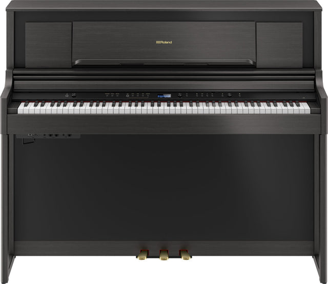 The image shows a Roland digital piano in a compact upright cabinet with a dark wood finish. It has a full 88-key weighted keyboard, a digital control panel with buttons and a small display, three pedals, and Roland branding on the music rack. This stylish, space-saving piano combines the feel of an acoustic piano with digital features like volume control and multiple voices, ideal for home use.