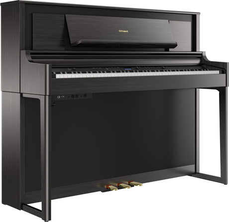 The image shows a Roland upright-style digital piano with a sleek dark wood finish. It features a full 88-key keyboard, three pedals, a digital control panel with buttons and a small display, a music rack, and the Roland logo on the top panel. Its modern, furniture-like design offers a space-efficient alternative to a grand piano while delivering an authentic piano playing experience with digital capabilities.