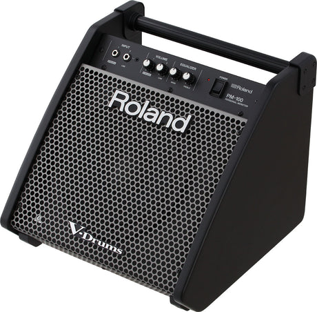 The image shows a Roland PM-100 Personal Monitor, a compact, wedge-shaped speaker designed for electronic drum kits (V-Drums). It features multiple input jacks, volume and EQ controls, a power switch, a protective mesh grille, and a carrying handle. Its angled design projects sound upward, providing electronic drummers with clear personal amplification for practice, rehearsal, or performance.