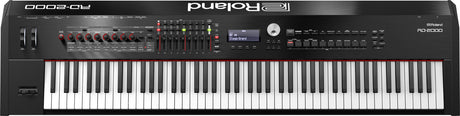 The image shows a Roland RD-2000 stage piano with a full 88-key weighted keyboard, a large display reading "Stage Grand," multiple red-rimmed rotary knobs, faders, buttons, LED indicators, and a data dial. It features a professional black finish and is designed for live performance and studio use, combining acoustic piano feel with advanced digital controls for professional musicians.