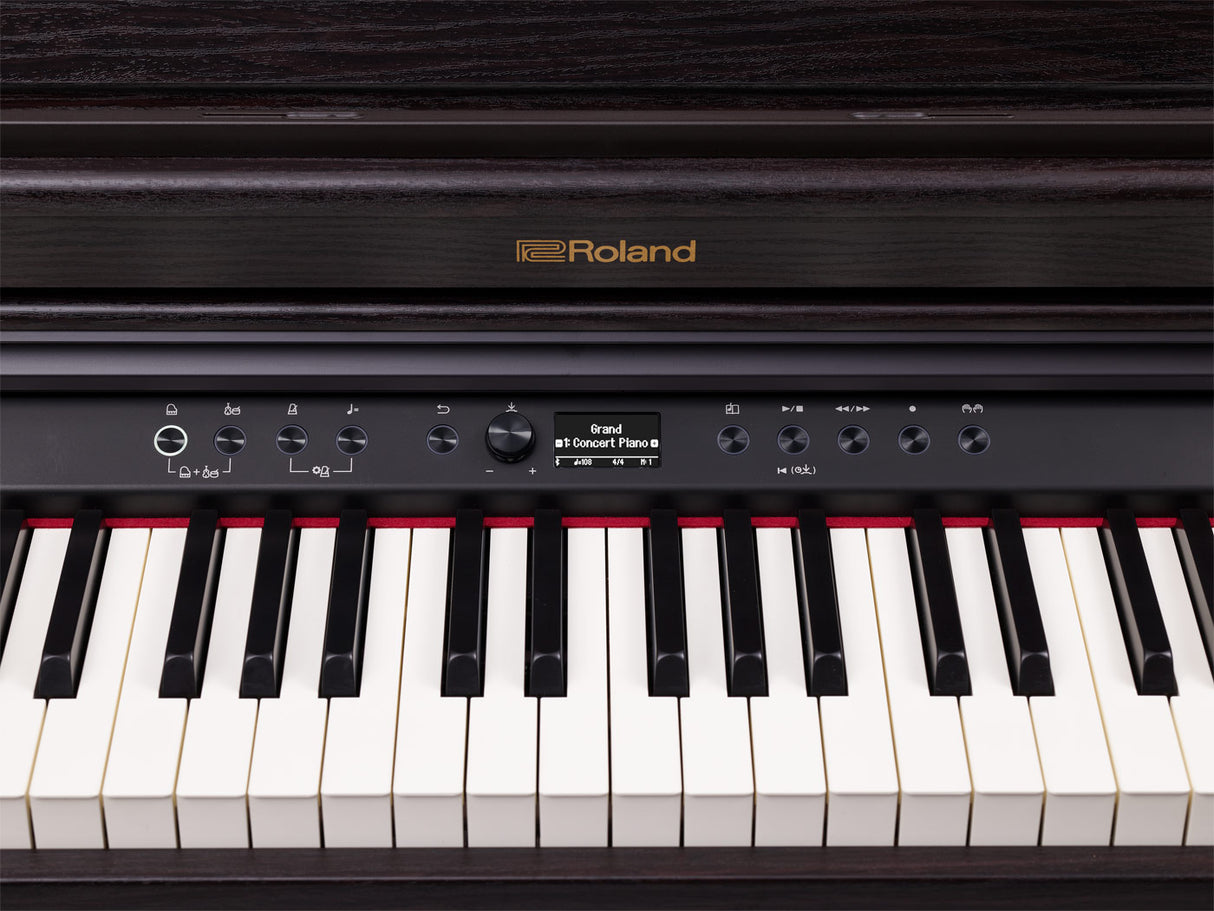 The image shows a Roland digital piano with the "Roland" logo in gold. It features a traditional 88-key layout, a control panel with rotary knobs, buttons, a digital display reading "Grand" and "Concert Piano," transport controls, and tempo functions. The instrument has a sleek black finish and a modern design, indicating a high-end model suited for home and professional use.