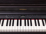 The image shows a Roland digital piano with the "Roland" logo in gold. It features a traditional 88-key layout, a control panel with rotary knobs, buttons, a digital display reading "Grand" and "Concert Piano," transport controls, and tempo functions. The instrument has a sleek black finish and a modern design, indicating a high-end model suited for home and professional use.