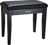 The image shows a Roland piano bench with a sleek black padded vinyl seat and four sturdy wooden legs. It features gold "Roland" branding on the front panel. Designed for comfort and proper posture, this bench is ideal for use with digital pianos, acoustic pianos, and keyboards. Known for stability and durability, it complements Roland’s electronic instruments or can be used with any piano setup.