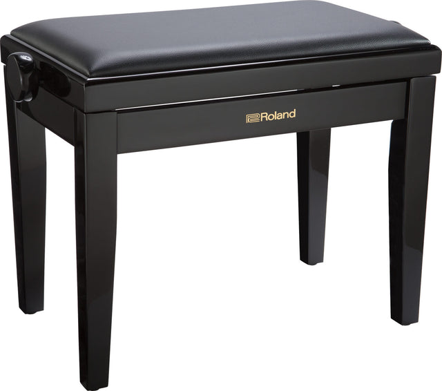 The image shows a Roland piano bench with a glossy black finish and gold logo on the front. It has a padded black seat, four sturdy wooden legs, and adjustable height knobs on the sides. The lift-up seat reveals storage space underneath. This adjustable bench provides comfort and proper posture for pianists and keyboard players.