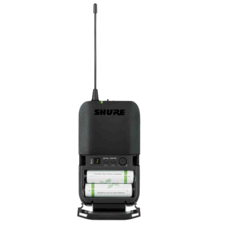 The image shows a Shure wireless bodypack transmitter with a black plastic housing and visible "SHURE" branding. It features an extendable antenna, an open battery compartment with two AA batteries, and a control panel with buttons and an LED indicator. This compact device wirelessly transmits audio from instruments or microphones, offering musicians freedom of movement during live performances.