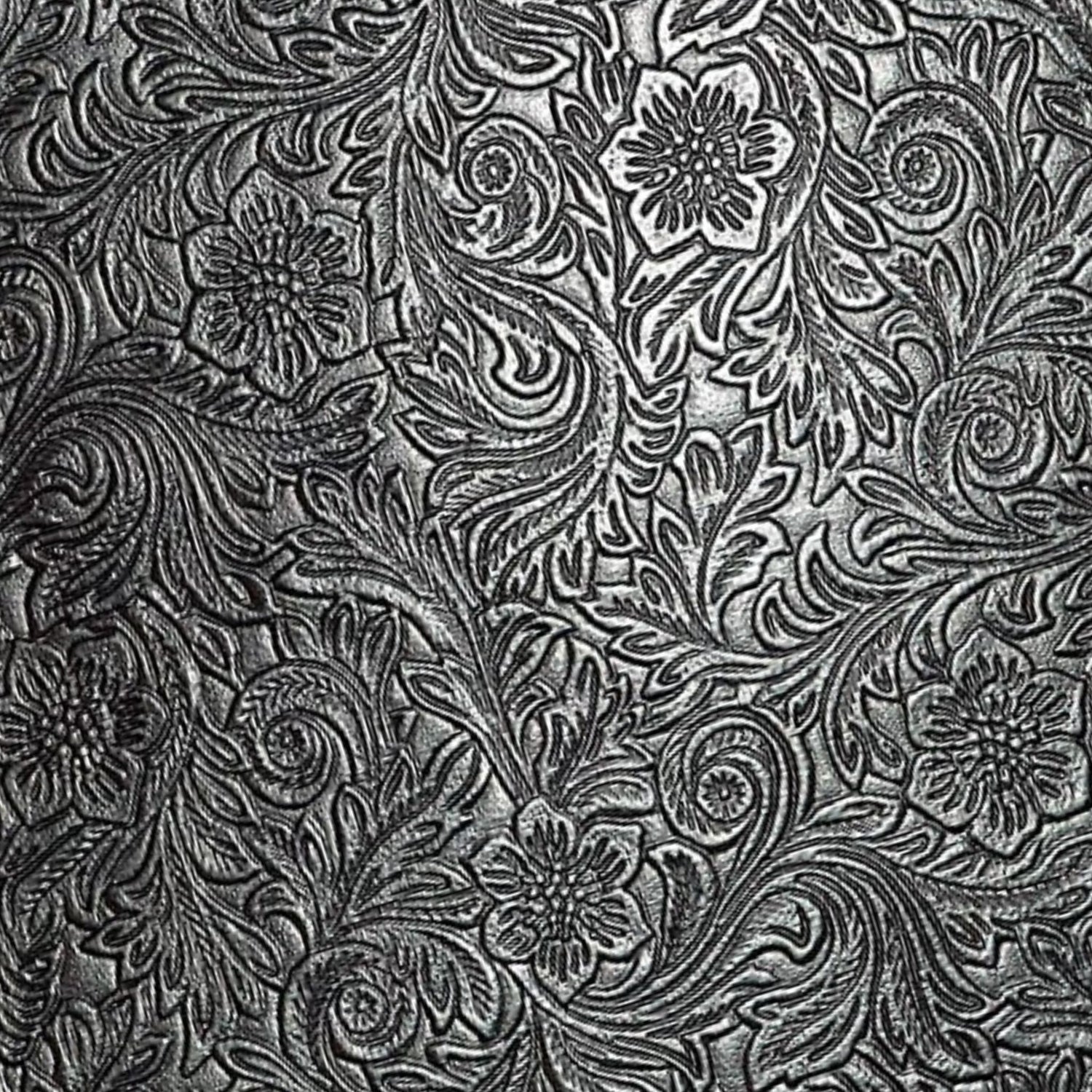 The image shows an ornate, tooled leather surface with intricate floral and scrollwork patterns in metallic silver against a dark background. This traditional embossed design is commonly found on musical instrument accessories like high-end guitar straps, vintage instrument cases, accordion bellows, banjo head surrounds, and premium music equipment bags, adding a functional yet elegant, vintage or western aesthetic.