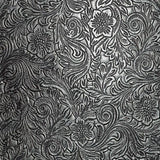 The image shows an ornate, tooled leather surface with intricate floral and scrollwork patterns in metallic silver against a dark background. This traditional embossed design is commonly found on musical instrument accessories like high-end guitar straps, vintage instrument cases, accordion bellows, banjo head surrounds, and premium music equipment bags, adding a functional yet elegant, vintage or western aesthetic.