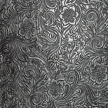The image shows an ornate, tooled leather surface with intricate floral and scrollwork patterns in metallic silver against a dark background. This traditional embossed design is commonly found on musical instrument accessories like high-end guitar straps, vintage instrument cases, accordion bellows, banjo head surrounds, and premium music equipment bags, adding a functional yet elegant, vintage or western aesthetic.