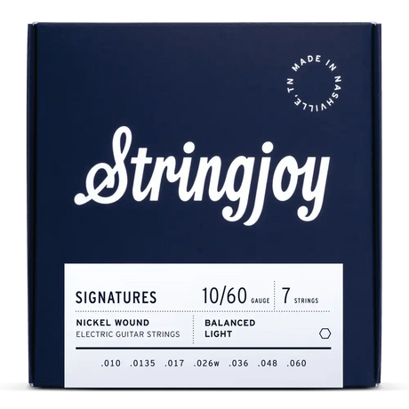 The image shows a package of Stringjoy "Signatures" 7-string electric guitar strings, gauge 10-60, nickel wound with balanced light tension. The deep navy box features white lettering, an elegant script logo, and "Made in Nashville, N.L." marking. This premium set is designed for extended range guitars, offering comfortable playability and tone across all seven strings.