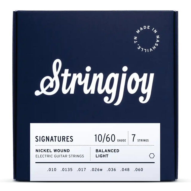 The image shows a package of Stringjoy "Signatures" 7-string electric guitar strings, gauge 10-60, nickel wound with balanced light tension. The deep navy box features white lettering, an elegant script logo, and "Made in Nashville, N.L." marking. This premium set is designed for extended range guitars, offering comfortable playability and tone across all seven strings.