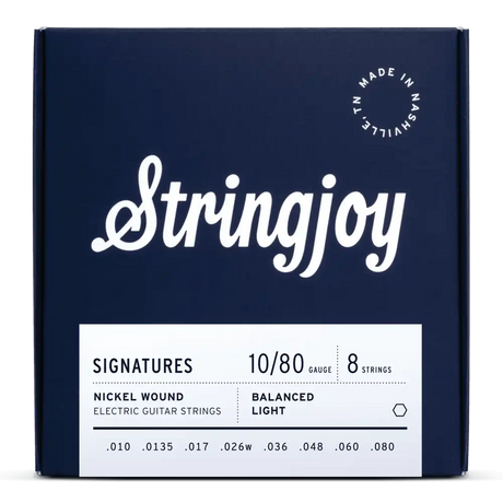 The image shows a navy blue package of Stringjoy "Signatures" 8-string electric guitar strings. The set features balanced light, nickel wound strings with gauges .010 to .080. The minimalist box includes white text and a "Made in Nashville, TN" logo. Designed for extended range guitars, it supports low tunings with a heavy .080 bass string.