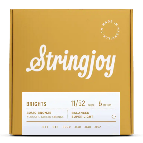 The image shows a package of Stringjoy "Brights" acoustic guitar strings in an attractive mustard yellow box. The set features 80/20 Bronze, super light gauge 11/52 strings (.011–.052) in a balanced 6-string configuration. The packaging highlights the brand name, product details, and a "Made in Nashville" badge, reflecting a premium, boutique quality product.