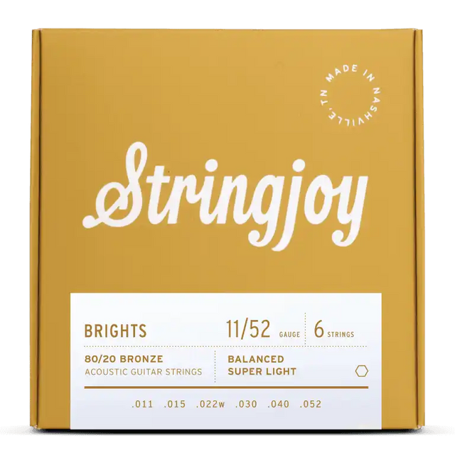 The image shows a package of Stringjoy "Brights" acoustic guitar strings in an attractive mustard yellow box. The set features 80/20 Bronze, super light gauge 11/52 strings (.011–.052) in a balanced 6-string configuration. The packaging highlights the brand name, product details, and a "Made in Nashville" badge, reflecting a premium, boutique quality product.