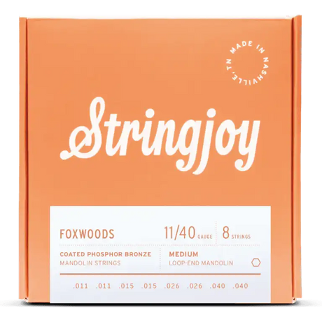 The image shows a package of Stringjoy Foxwoods Coated Phosphor Bronze mandolin strings in medium gauge 11/40. It contains 8 medium loop-end strings (.011, .011, .015, .015, .026, .026, .040, .040) in a coral-orange box with white script branding. A "Made in Nashville" logo appears in the top right, and product details are on a white label at the bottom. The coated strings offer enhanced tone and durability.