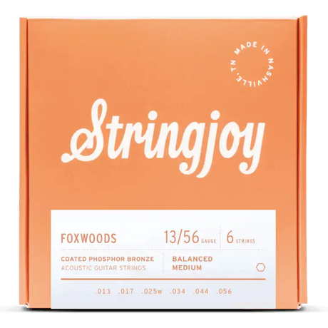 The image shows a package of Stringjoy Foxwoods coated phosphor bronze acoustic guitar strings. The orange/coral box features white lettering with the Stringjoy logo in script font. It’s a 6-string set, gauge 13/56, balanced medium tension, with gauges .013 to .056. A "Made in Nashville" badge indicates American-made quality. The coated strings offer warm tone and durability.