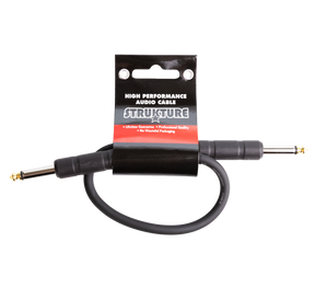 The image shows a STRUKTURE high-performance audio patch cable with gold-plated 1/4" TS/TRS connectors. It is a short, black professional-grade cable, likely 6-12 inches long, designed for connecting effects pedals or instruments to amplifiers. The cable features a lifetime guarantee, professional quality, and eco-friendly packaging, appealing to musicians seeking reliable, low-noise audio connections.