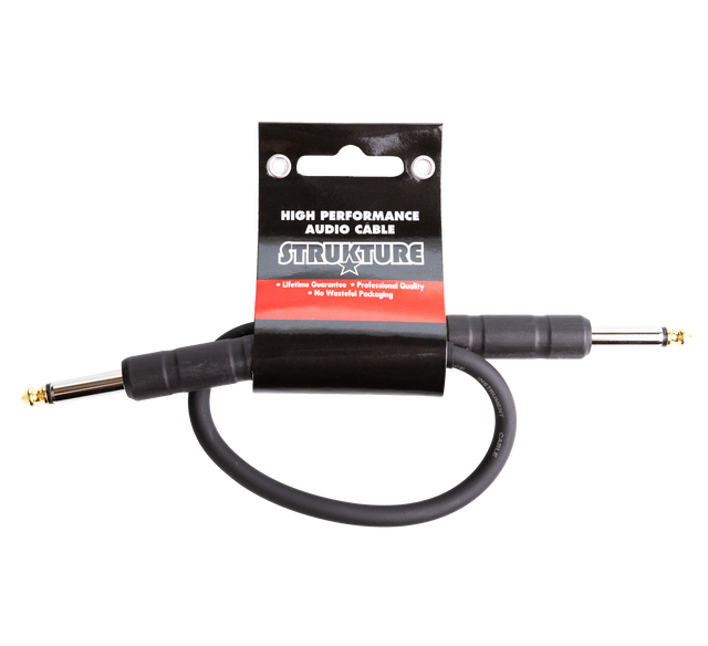 The image shows a STRUKTURE high-performance audio patch cable with gold-plated 1/4" TS/TRS connectors. It is a short, black professional-grade cable, likely 6-12 inches long, designed for connecting effects pedals or instruments to amplifiers. The cable features a lifetime guarantee, professional quality, and eco-friendly packaging, appealing to musicians seeking reliable, low-noise audio connections.