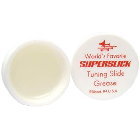 The image shows a container of Superslick Tuning Slide Grease, a specialized lubricant for brass instruments like trumpets, trombones, and tubas. The small white plastic jar with a red-labeled lid is open to reveal cream-colored grease inside. Made in Elkhart, Indiana, it helps tuning slides move smoothly for proper pitch adjustment, preventing sticking and ensuring the instrument stays in good condition.