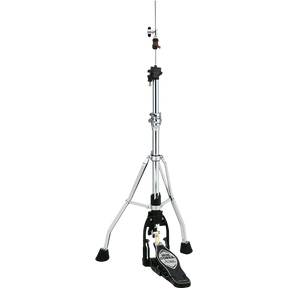 The image shows a hi-hat cymbal stand with a tall, adjustable chrome post, sturdy tripod base with rubber feet, and a black foot pedal featuring a brand logo. It includes clamps and adjustment mechanisms along the post. This essential drum hardware holds hi-hat cymbals (not shown) and allows drummers to control cymbal tension and create varied sounds from tight "chick" to open crashes.