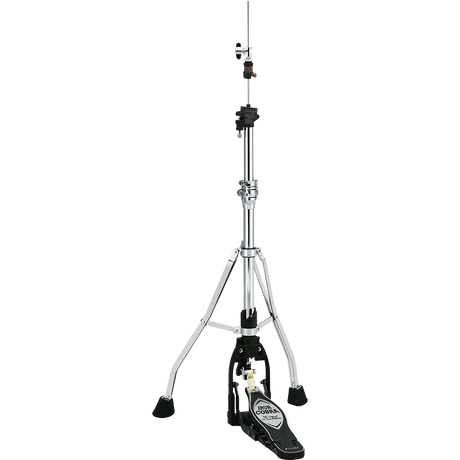 The image shows a hi-hat cymbal stand with a tall, adjustable chrome post, sturdy tripod base with rubber feet, and a black foot pedal featuring a brand logo. It includes clamps and adjustment mechanisms along the post. This essential drum hardware holds hi-hat cymbals (not shown) and allows drummers to control cymbal tension and create varied sounds from tight "chick" to open crashes.