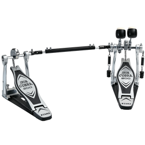 The image shows a Tama Iron Cobra 200 series double bass drum pedal with two connected foot pedals and a chain drive system. It features chrome and black metal construction, adjustable black beaters, wide footplates for stability, and branding on the pedal plates. Designed for fast, complex bass drum patterns, it’s popular in rock and metal for smooth, durable performance.