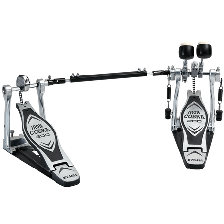 The image shows a Tama Iron Cobra 200 series double bass drum pedal with two connected foot pedals and a chain drive system. It features chrome and black metal construction, adjustable black beaters, wide footplates for stability, and branding on the pedal plates. Designed for fast, complex bass drum patterns, it’s popular in rock and metal for smooth, durable performance.