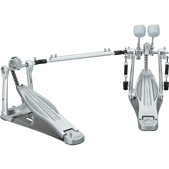 The image shows a high-end double bass drum pedal with dual foot pedals connected by a drive shaft, featuring chain or belt drive, adjustable white/felt beaters, sturdy metal frame, spring returns, and customizable tension and positioning. Made by Tama, this professional-grade pedal enables drummers to play fast, complex bass drum patterns used in metal, rock, and jazz.