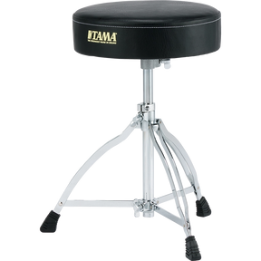 The image shows a Tama drum throne with a round, padded black seat featuring the gold "TAMA" logo and slogan. It has an adjustable chrome center post, a sturdy tripod base with rubber feet, and heavy-duty hardware. This professional drum stool offers comfort, stability, and ergonomic support, making it essential for drummers to maintain good posture and play comfortably.