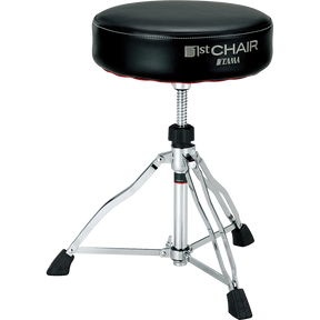 The image shows a Tama drum throne from the "1st Chair" series with a round, padded black vinyl seat. It features an adjustable height threaded rod, a sturdy chrome tripod base with rubber feet for stability, and professional-grade construction. This durable stool provides comfort and optimal seating for drummers during long sessions, reflecting Tama’s reputation for high-quality percussion accessories.
