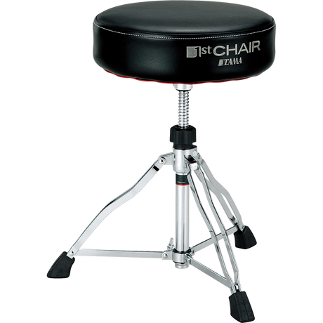 The image shows a Tama drum throne from the "1st Chair" series with a round, padded black vinyl seat. It features an adjustable height threaded rod, a sturdy chrome tripod base with rubber feet for stability, and professional-grade construction. This durable stool provides comfort and optimal seating for drummers during long sessions, reflecting Tama’s reputation for high-quality percussion accessories.