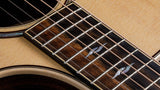 The image shows a close-up of an acoustic guitar focusing on the sound hole, fretboard, and strings. Visible elements include the circular sound hole with decorative rosette, six steel strings, metal frets, dark wood fretboard with position markers, and light-colored soundboard. The guitar features clean craftsmanship and natural wood tones, reflecting a well-made, versatile instrument suited for various musical styles.
