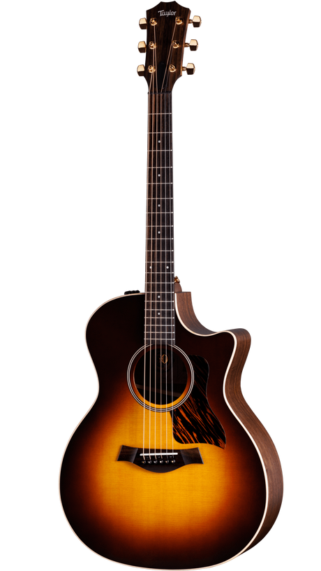 The image shows a Taylor acoustic-electric guitar with a Grand Auditorium cutaway body. It features a sunburst finish, dark wood back and sides, a round soundhole with rosette, tortoiseshell pickguard, and gold tuning machines. The dark fretboard has dot markers, and the cutaway allows easy access to higher frets. This high-end model highlights premium craftsmanship and materials typical of Taylor Guitars.