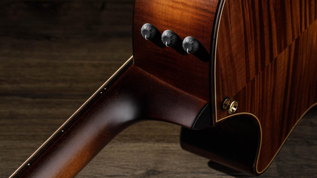 The image shows a high-quality acoustic-electric guitar with a rich brown wood finish and visible grain patterns. It features a traditional round sound hole, three black control knobs for volume and tone, decorative binding along the edges, and a professional finish, indicating careful craftsmanship and a higher-end instrument designed for amplified performance.