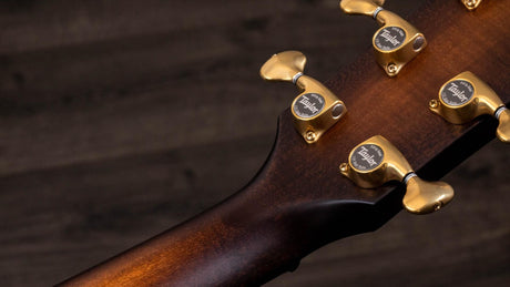 The image shows the headstock of a high-end acoustic guitar featuring four gold Taylor tuning machines. The rich brown wood grain, likely mahogany, highlights fine craftsmanship with smooth curves and professional finishing. The gold hardware combines functional precision tuning with elegant design, reflecting Taylor's reputation for premium, professional-grade acoustic guitars.