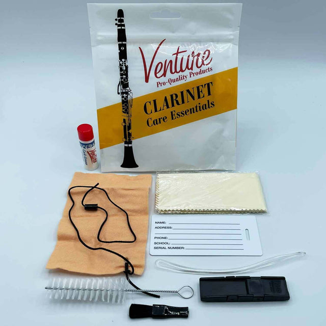 The image shows a Venture Pro-Quality clarinet care kit containing essential maintenance items: a branded clear plastic bag, a small bottle of key oil with a red cap, a tan cleaning cloth with a black pull string, a cleaning swab in packaging, a flexible cleaning rod, a small brush, a black reed case or accessory, and an identification tag for personal info. This kit helps players clean and maintain their clarinet properly.